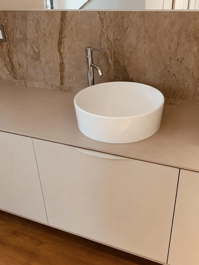 Vasque à poser ronde sur un plan de toilette en pierre, meubles blancs et parquet